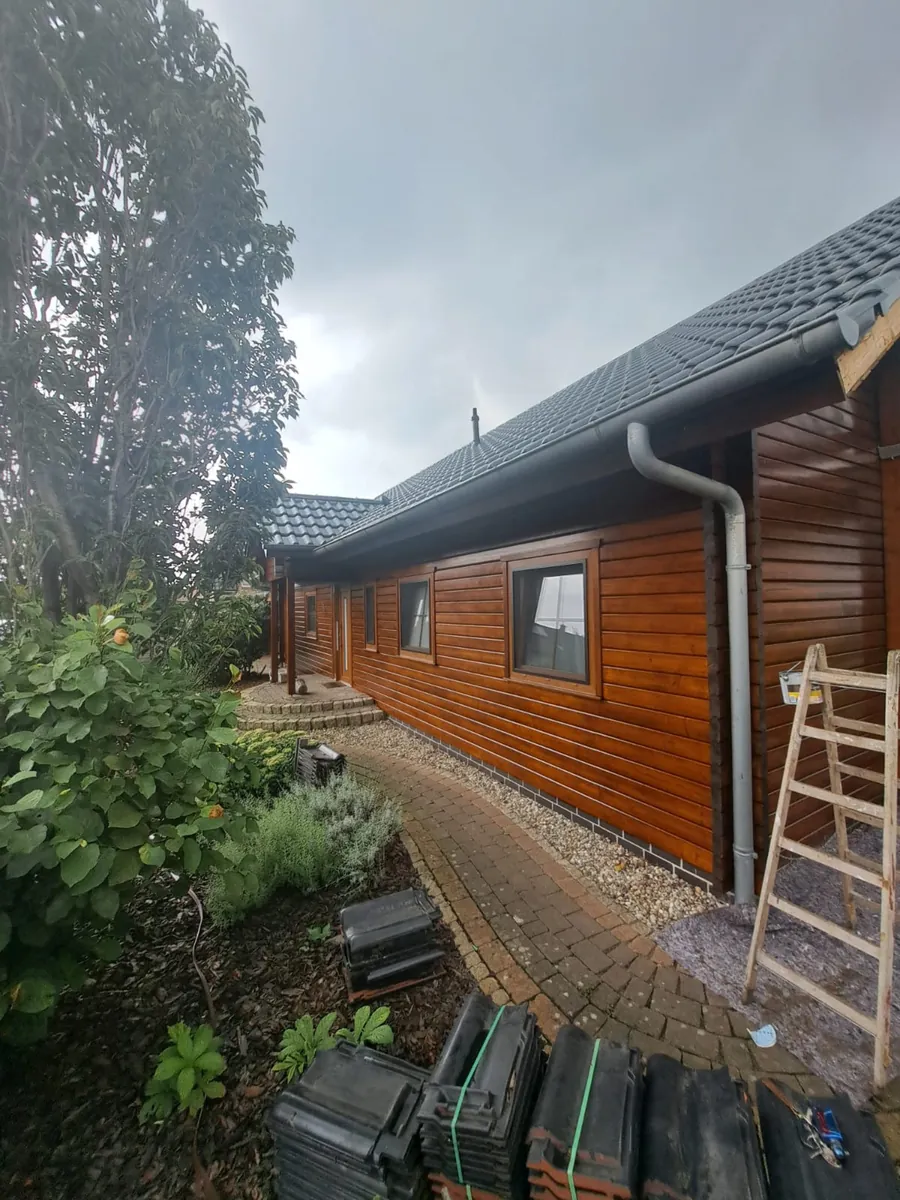 Holzhaus mit neu lasierter Fassade, davor die Leiter der Malerarbeiten